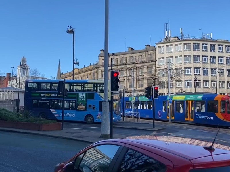A view of Sheffield city centre with a car in the foreground, bus in the middle ground along with a Supertram, in the background are some office type buildings