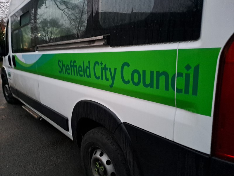 The side of a white minibus with green Sheffield City Council branding down the side