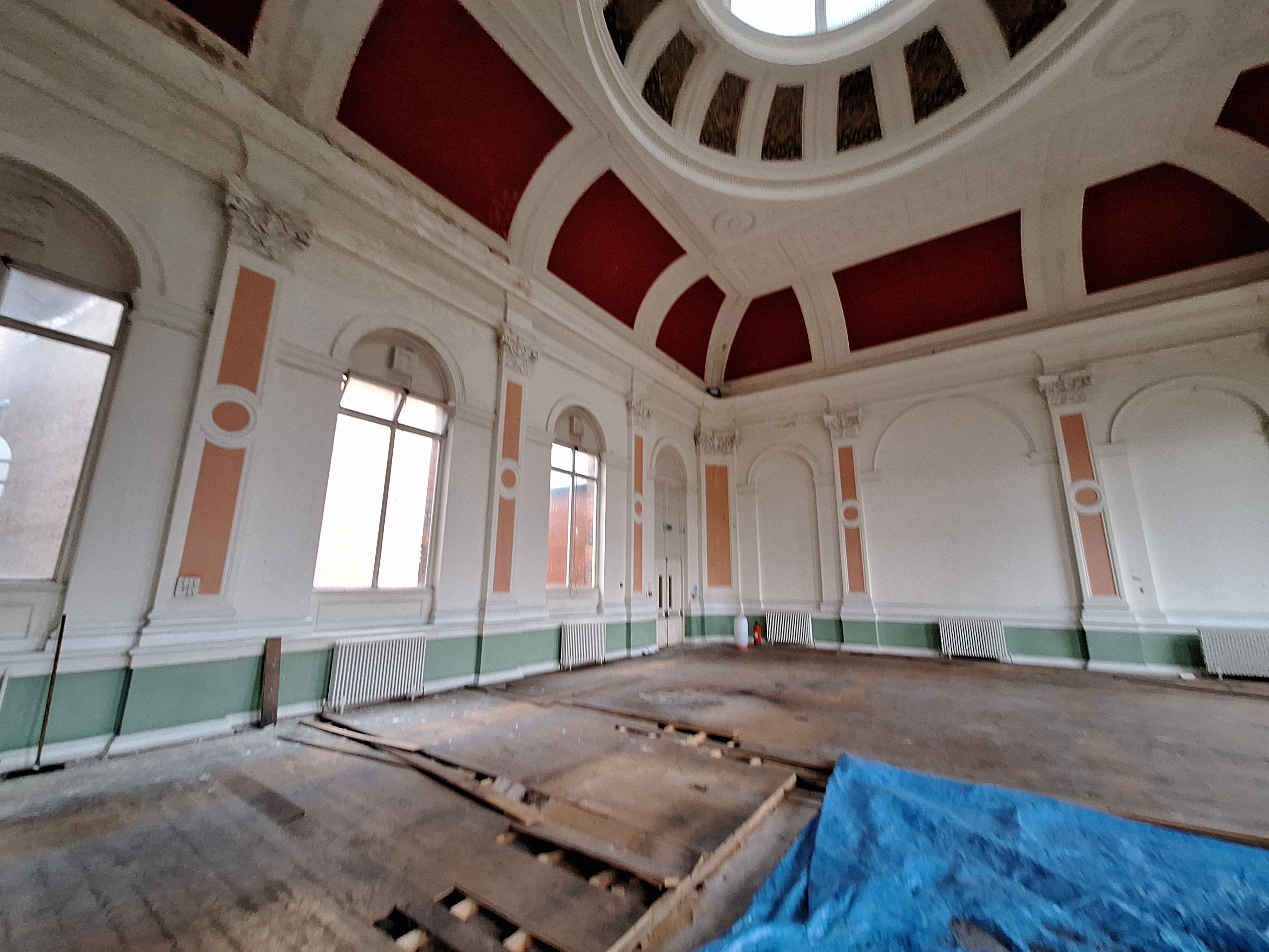 Grand interior of Canada House with high red and white ceilings, large windows and damaged floor boards covered in blue sheets