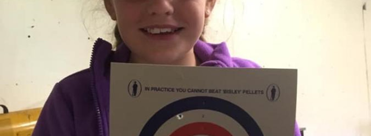 Young girl holding a shooting target full of holes up and smiling