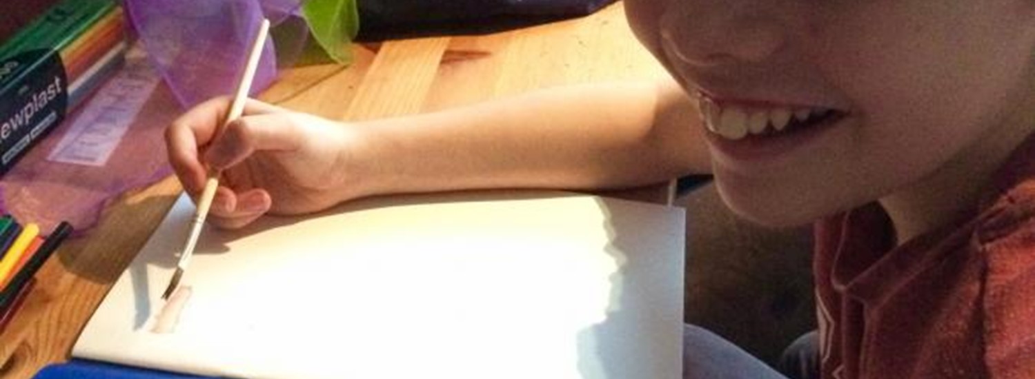 A child drawing at a desk surrounded by art materials