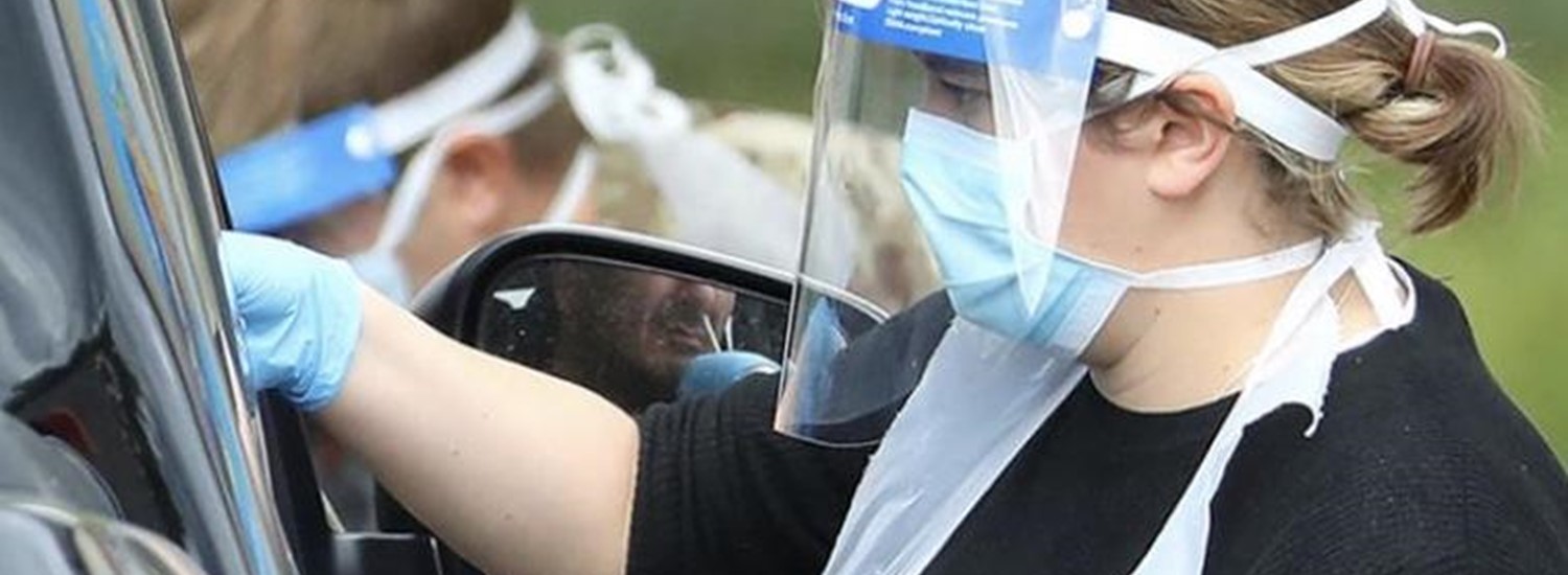 Woman in PPE testing someone for Covid-19 through car window