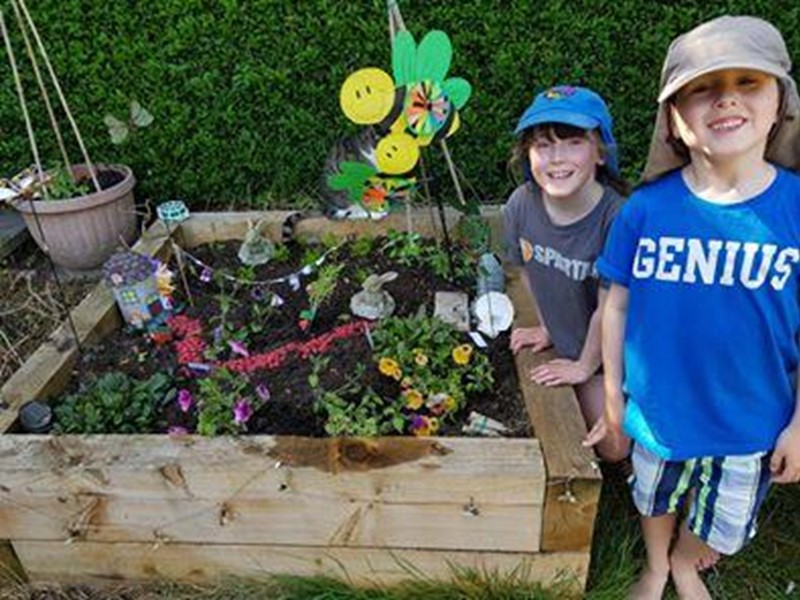 Two boys stand next to a fairy garden they have made