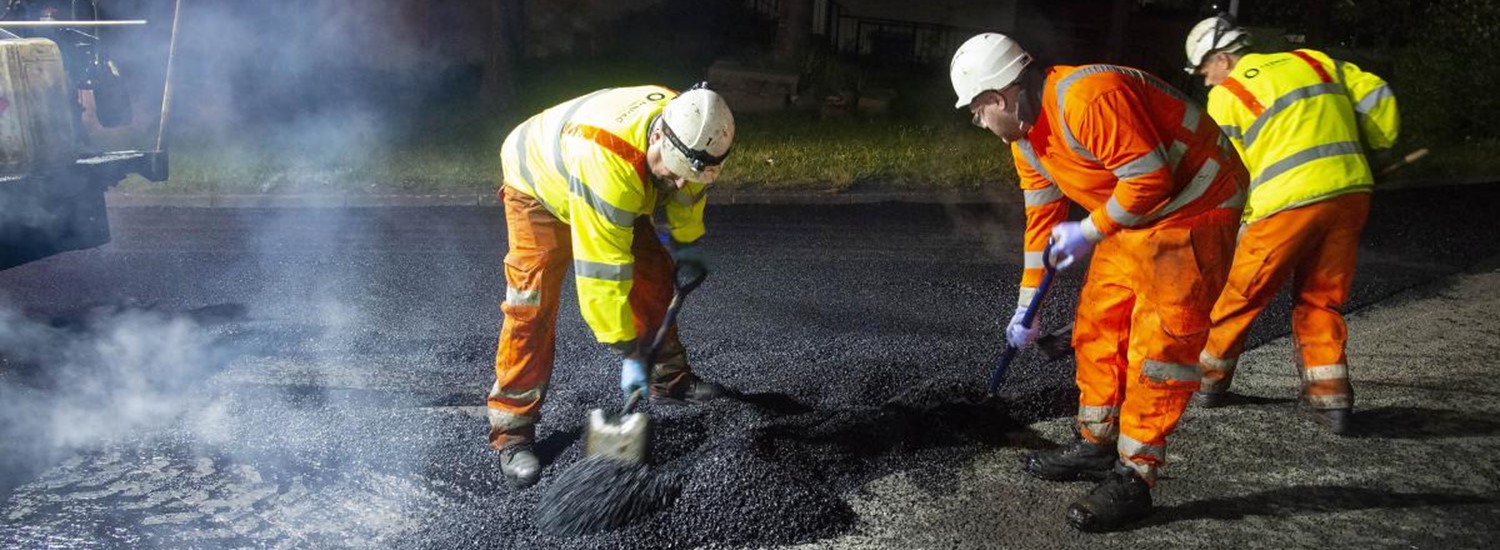 A photograph of workmen shovelling tarmac on to a road