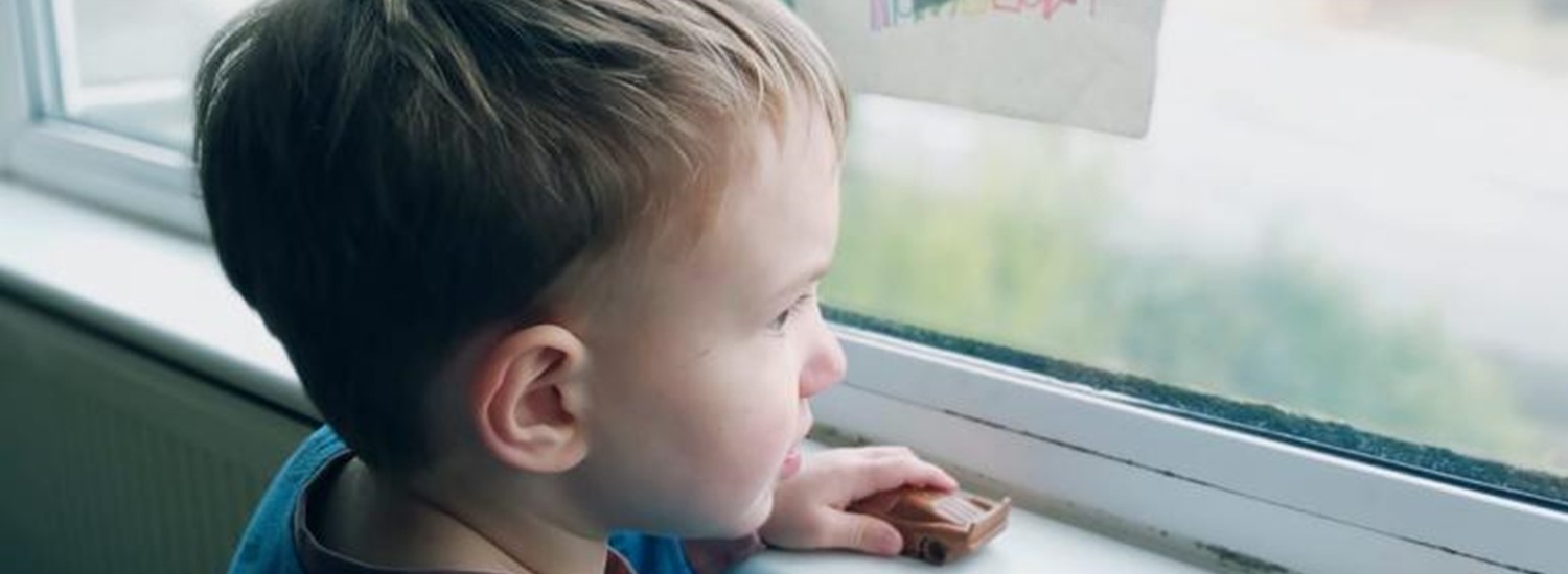 Young boy looks out of a window decorated with a rainbow