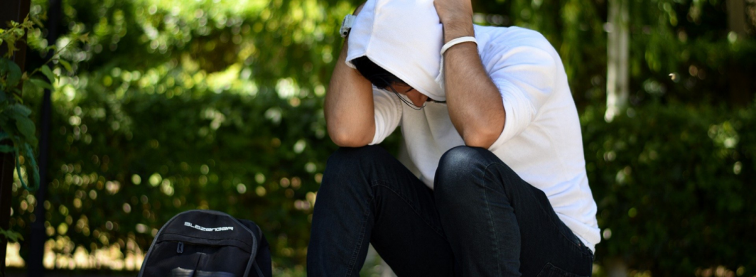 Man sitting with head in hands and hood up