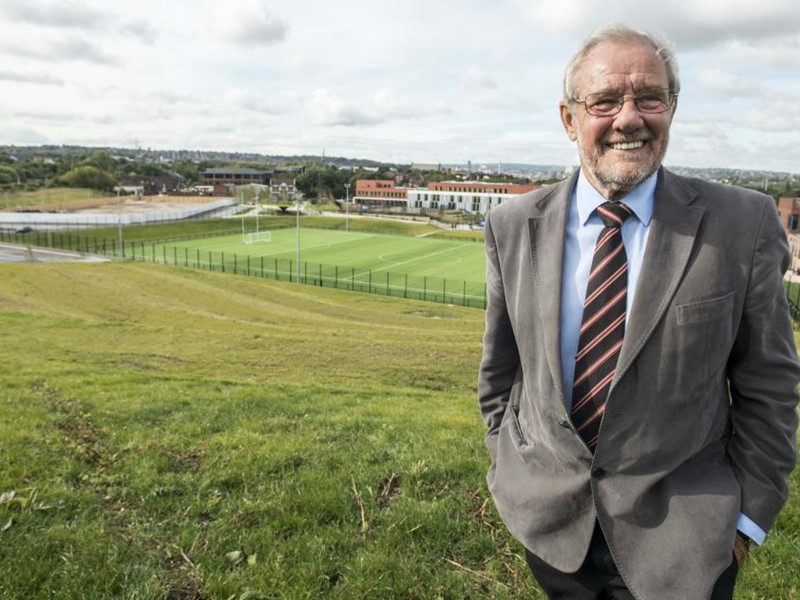 A man wearing a grey suit standing on a grassed field